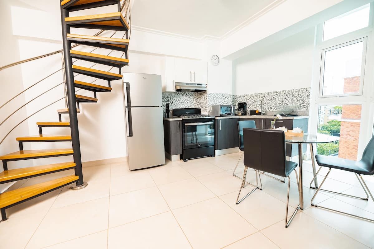 Een moderne keuken met een spiltrap, een eethoek met twee stoelen en uitzicht door een groot raam.