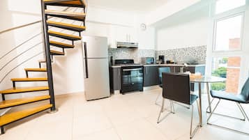 A modern kitchen with a spiral staircase, a dining area with two chairs, and a view through a large window.