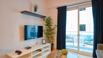Uma sala de estar moderna com televisão de tela plana, um rack branco, uma planta em vaso e uma varanda com mobiliário de exterior.