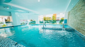 An indoor swimming pool with clear blue water, tiled edges, and a water fountain. - Central Park Tower (Santo Domingo)