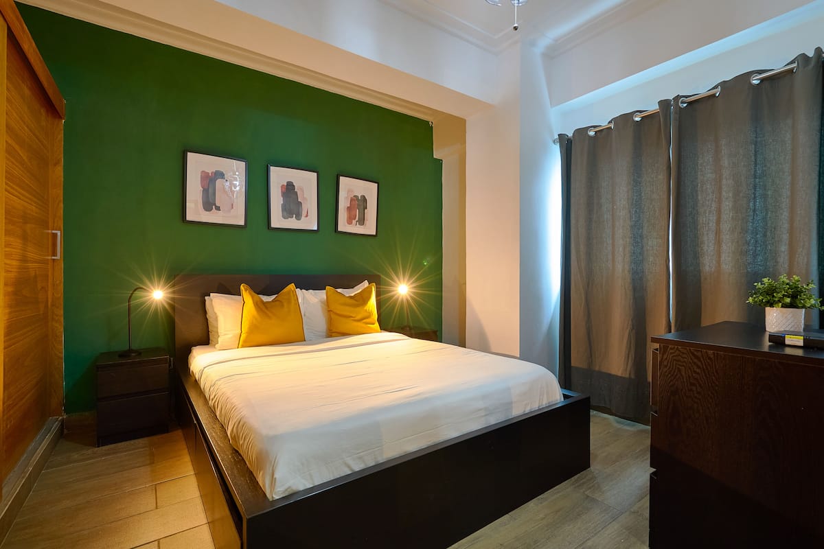 Een slaapkamer met een bed, groene wanden, ingelijste foto's en een nachtkastje.