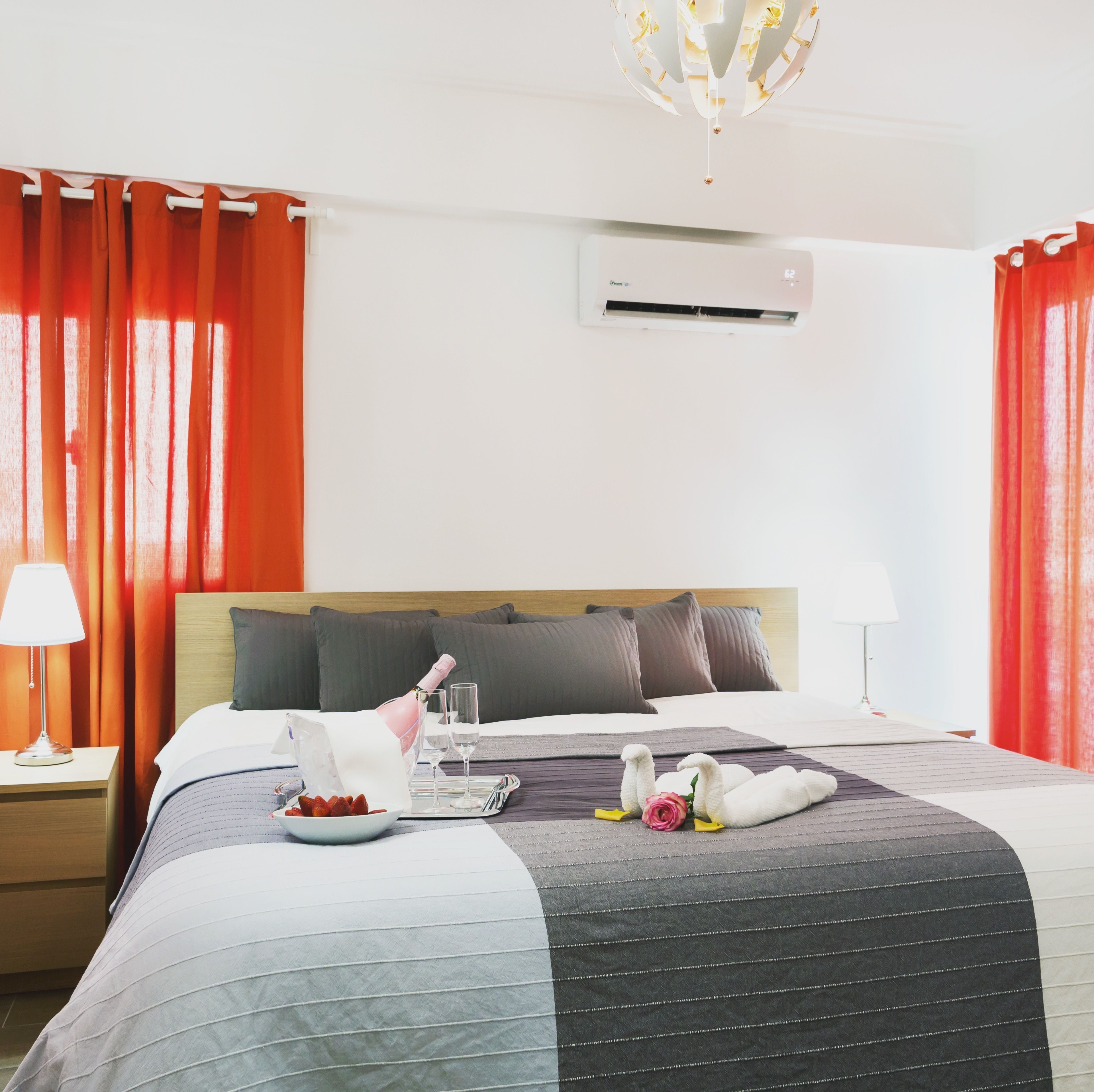 Una habitación de hotel con una cama, una mesita de noche, una lámpara, una botella de champán, dos copas de vino, una bandeja con fresas y adornos con forma de cisnes.