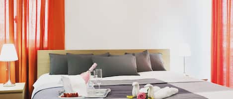 A hotel room with a bed, a nightstand, a lamp, a bottle of champagne, two wine glasses, a tray with strawberries, and decorative swans.