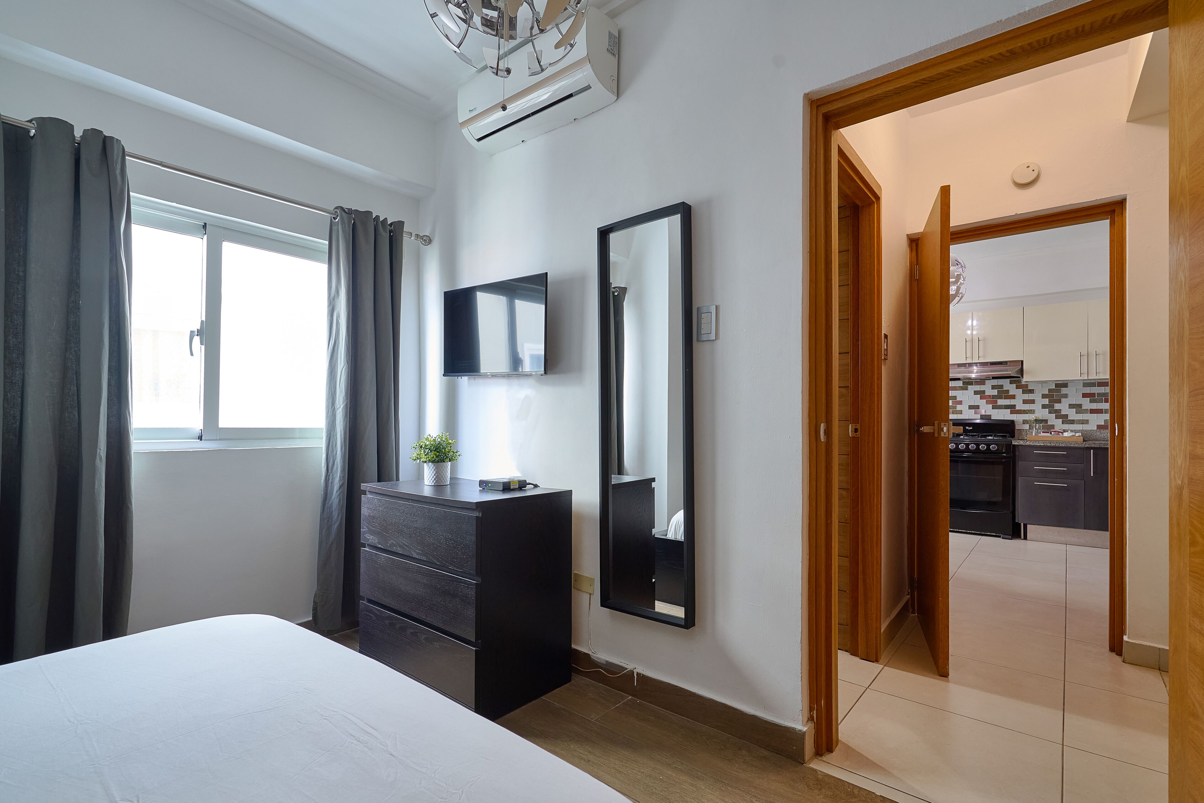 Une chambre à coucher avec un lit, une commode, un miroir et une fenêtre avec des rideaux.