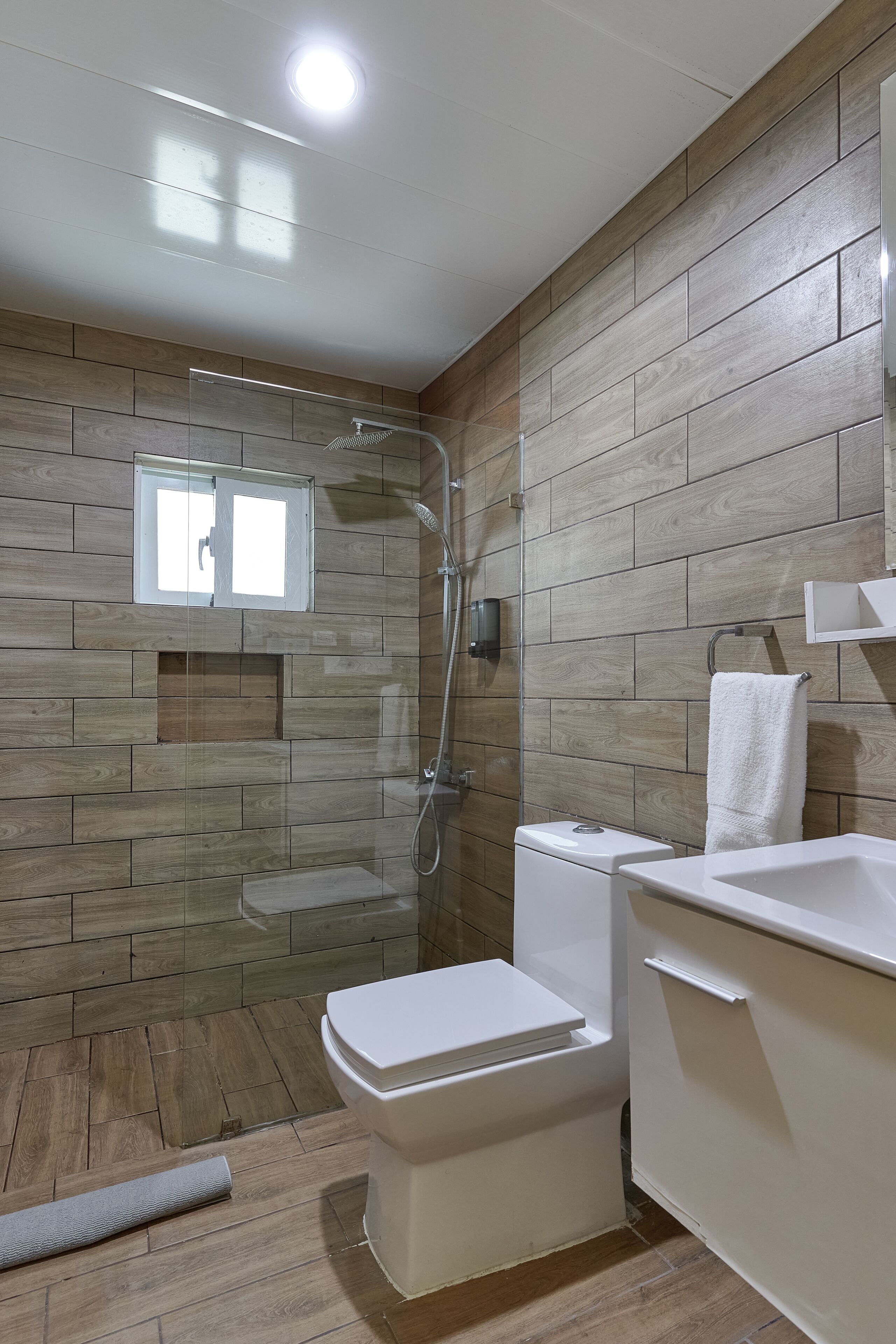 Ein Badezimmer mit Holzpaneelen, einer Duschkabine, einer Toilette und einem Waschbecken, an der Wand hängt ein Handtuch.