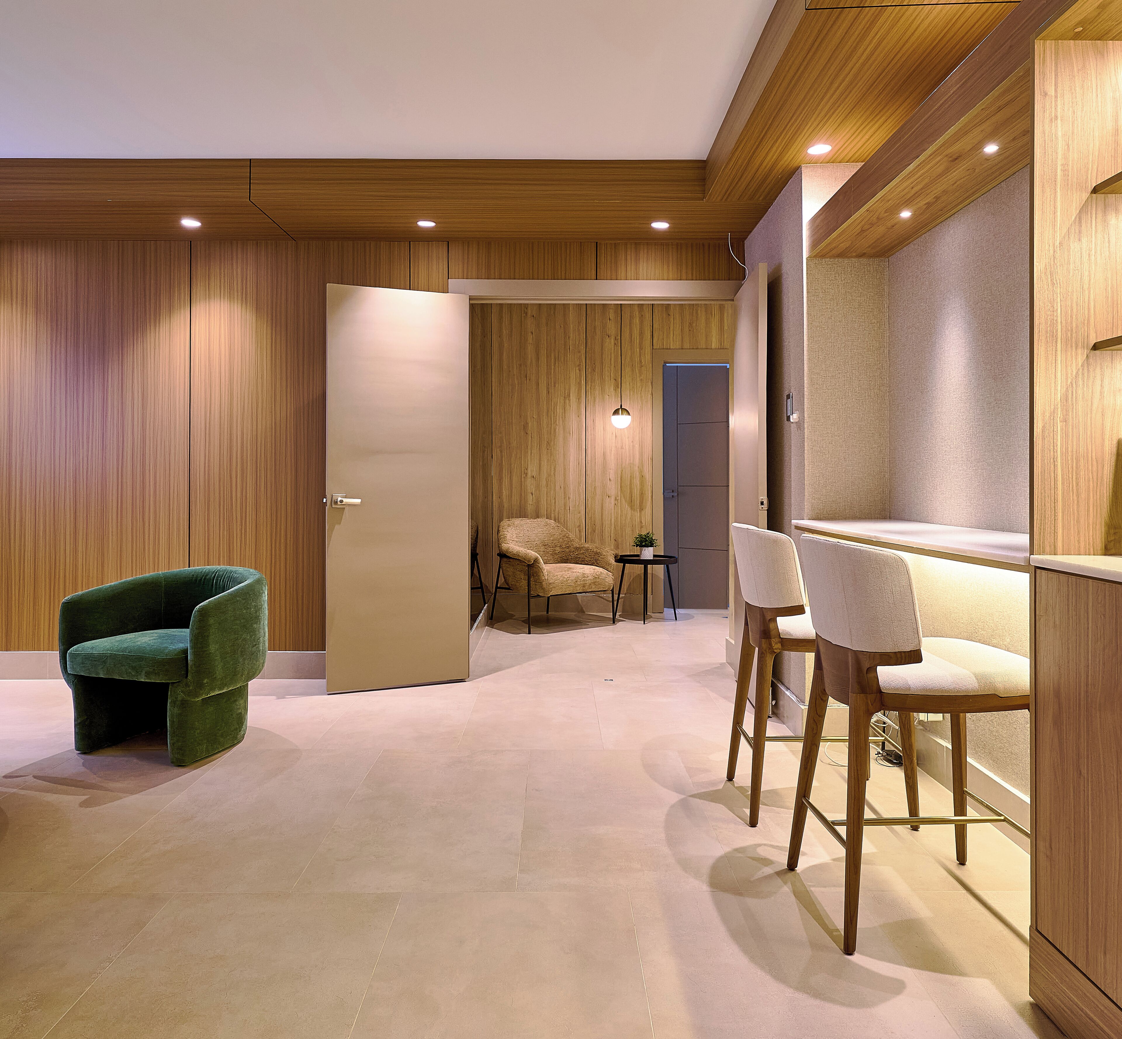 A modern interior with a wooden ceiling, a green armchair, two white chairs, and a small table with a plant.