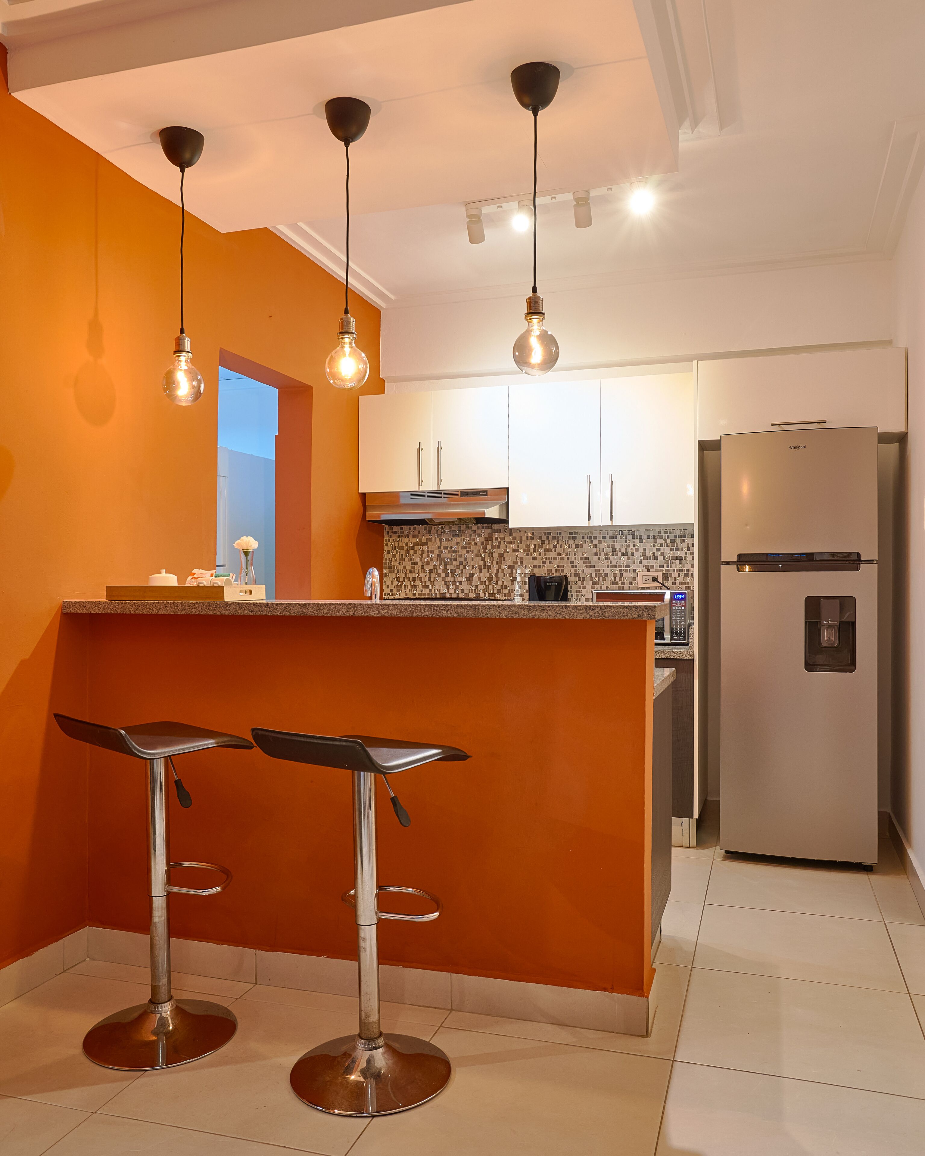 A modern kitchen with a central island, bar stools, a refrigerator, and pendant lighting.
