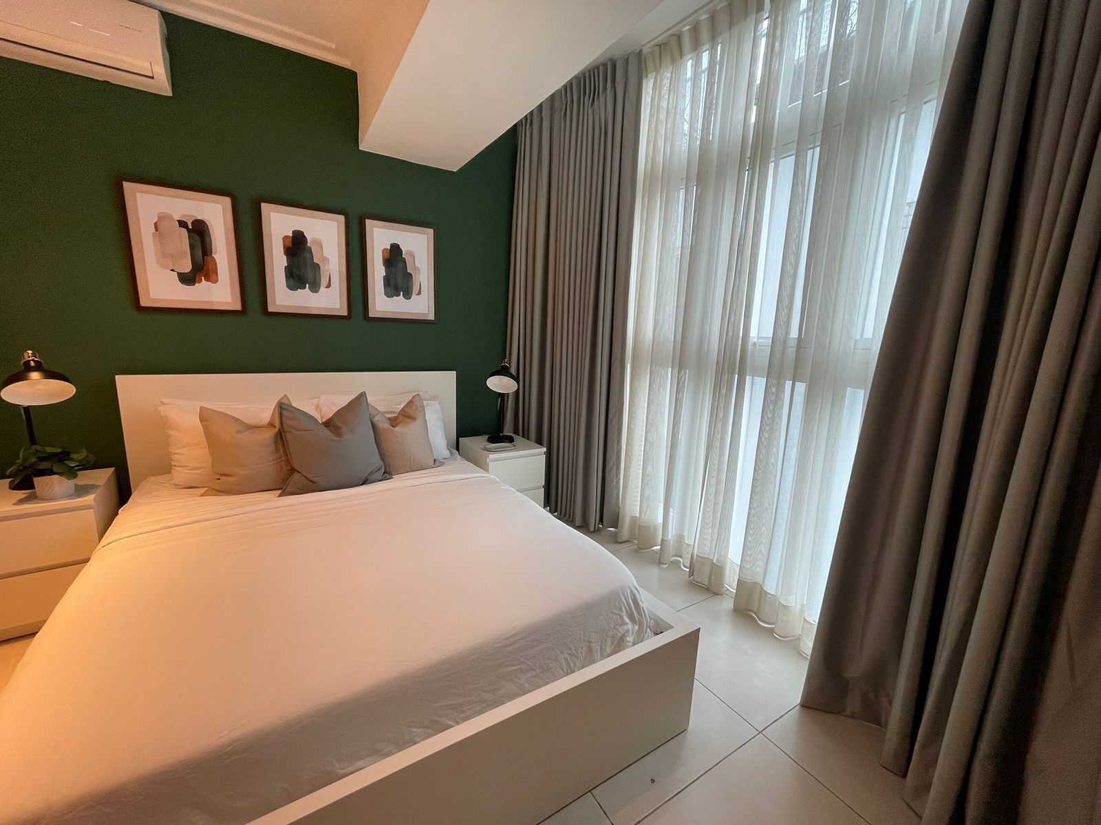 A modern bedroom with a large bed, two bedside tables, and three framed artworks on the wall.
