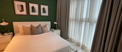 A modern bedroom with a large bed, two bedside tables, and three framed artworks on the wall.