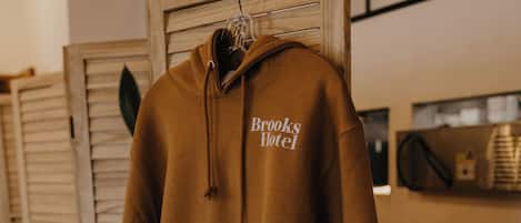 Een bruine hoodtrui met de tekst 'Brooks Hotel' hangend aan een houten rek.