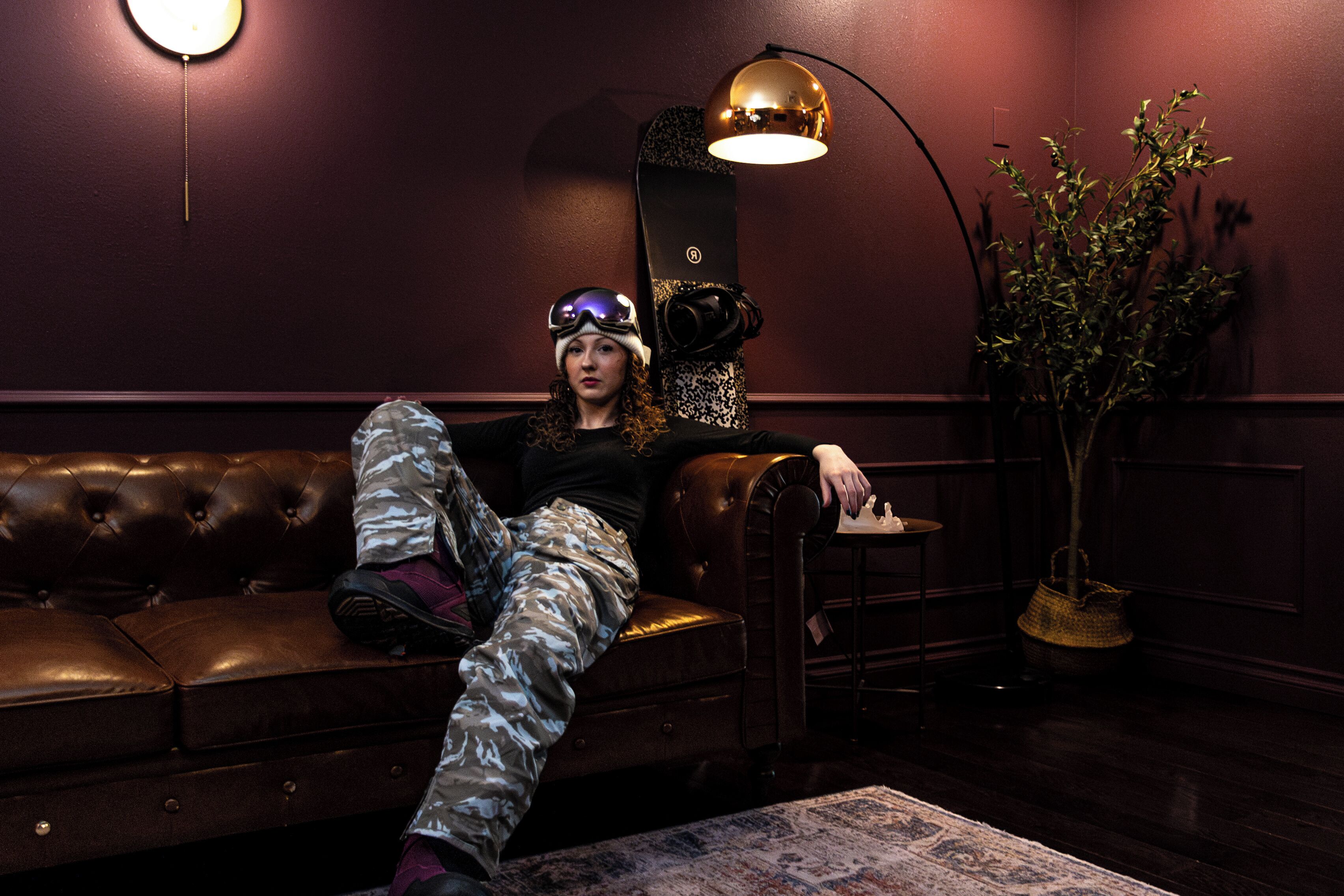 A person seated on a leather sofa in a room with a dark wall, a lamp, and a plant.