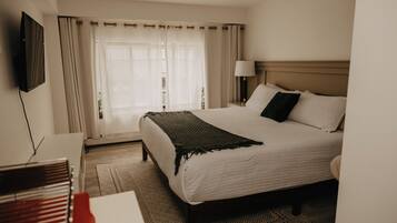 Habitación de hotel con cama, televisión, escritorio y teclado, y ventana con cortinas.