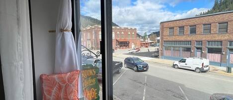 A view from a window with a pillow on a bench, a street with cars, and buildings in the background.