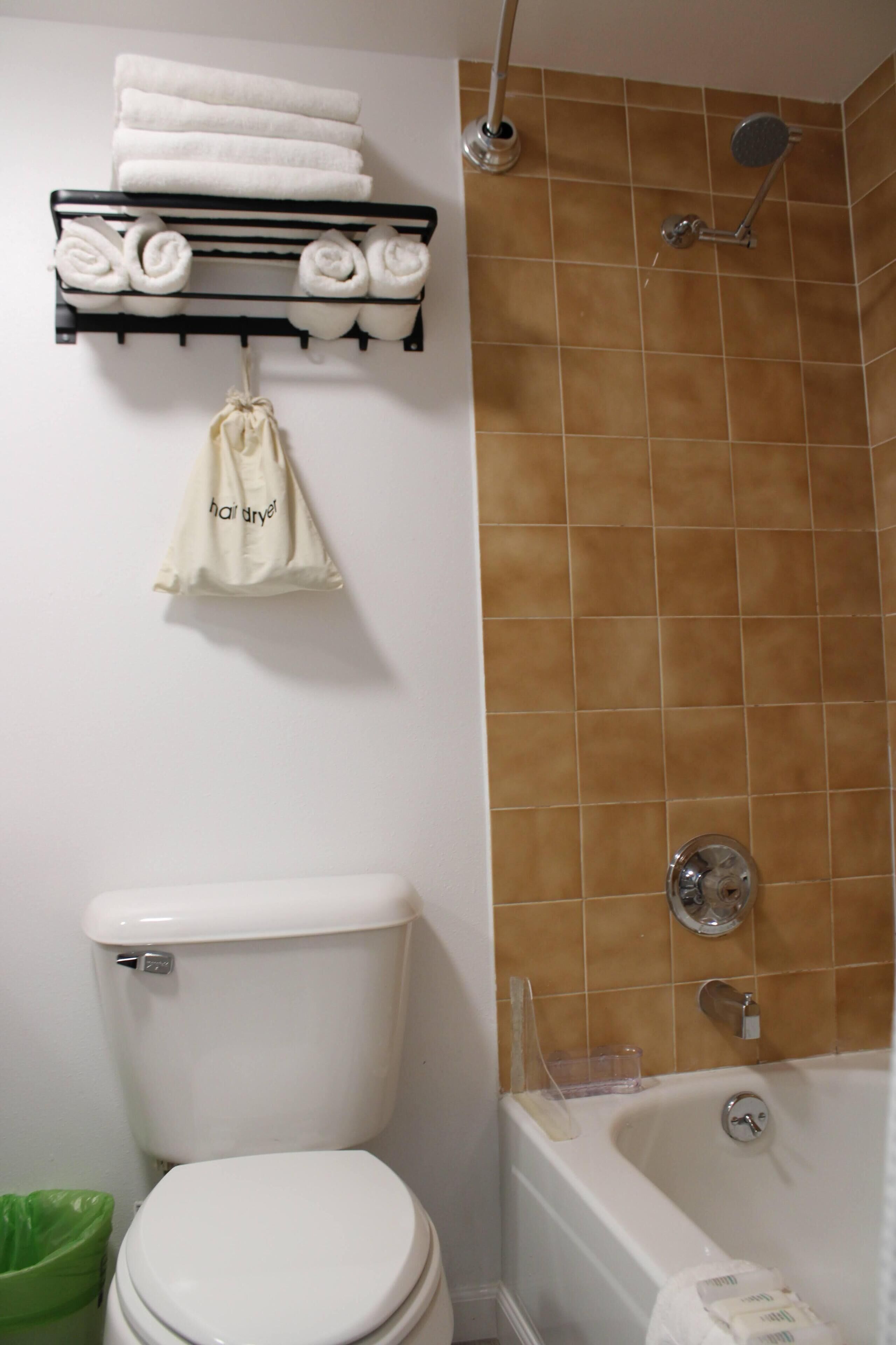 Un baño con inodoro, ducha y toallero con toallas dobladas.