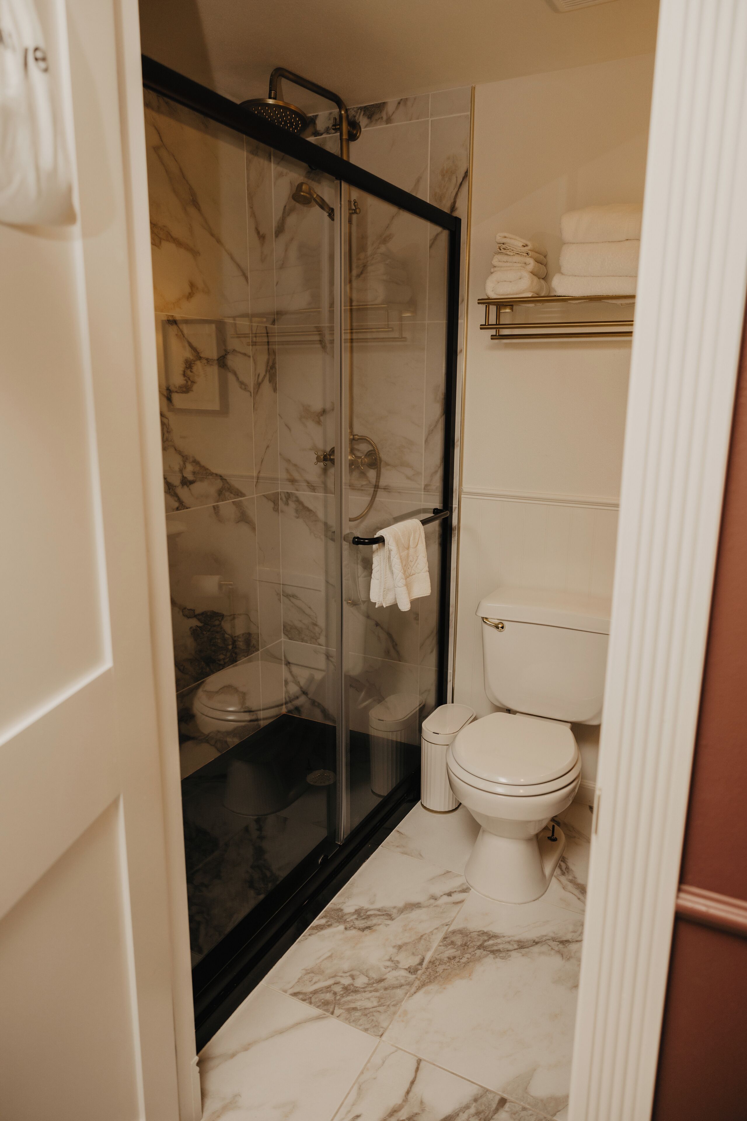 Baño con ducha envuelta en vidrio, inodoro y suelo de mármol.