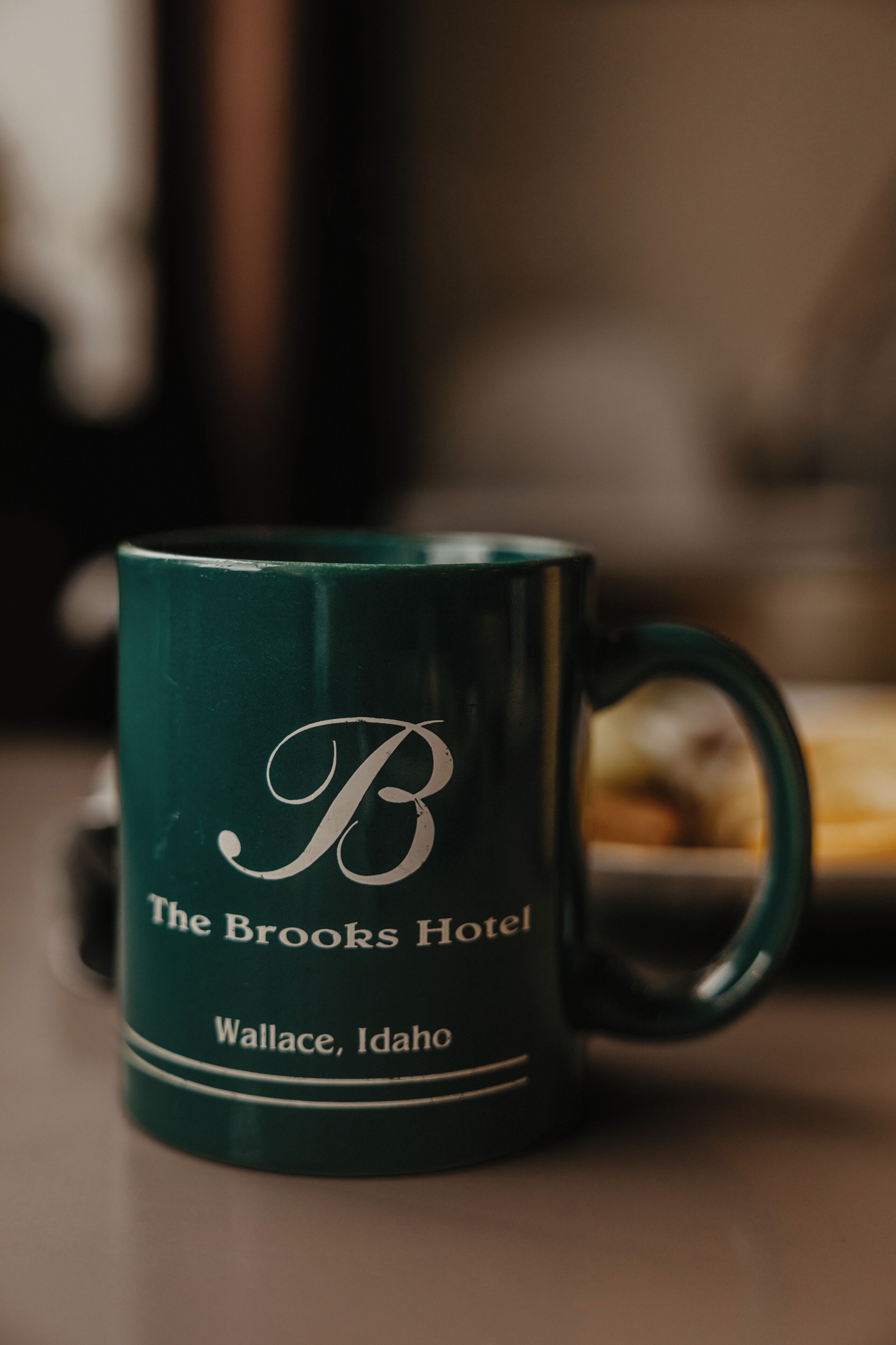 A green mug with a logo and text indicating it is from The Brooks Hotel in Wallace, Idaho.