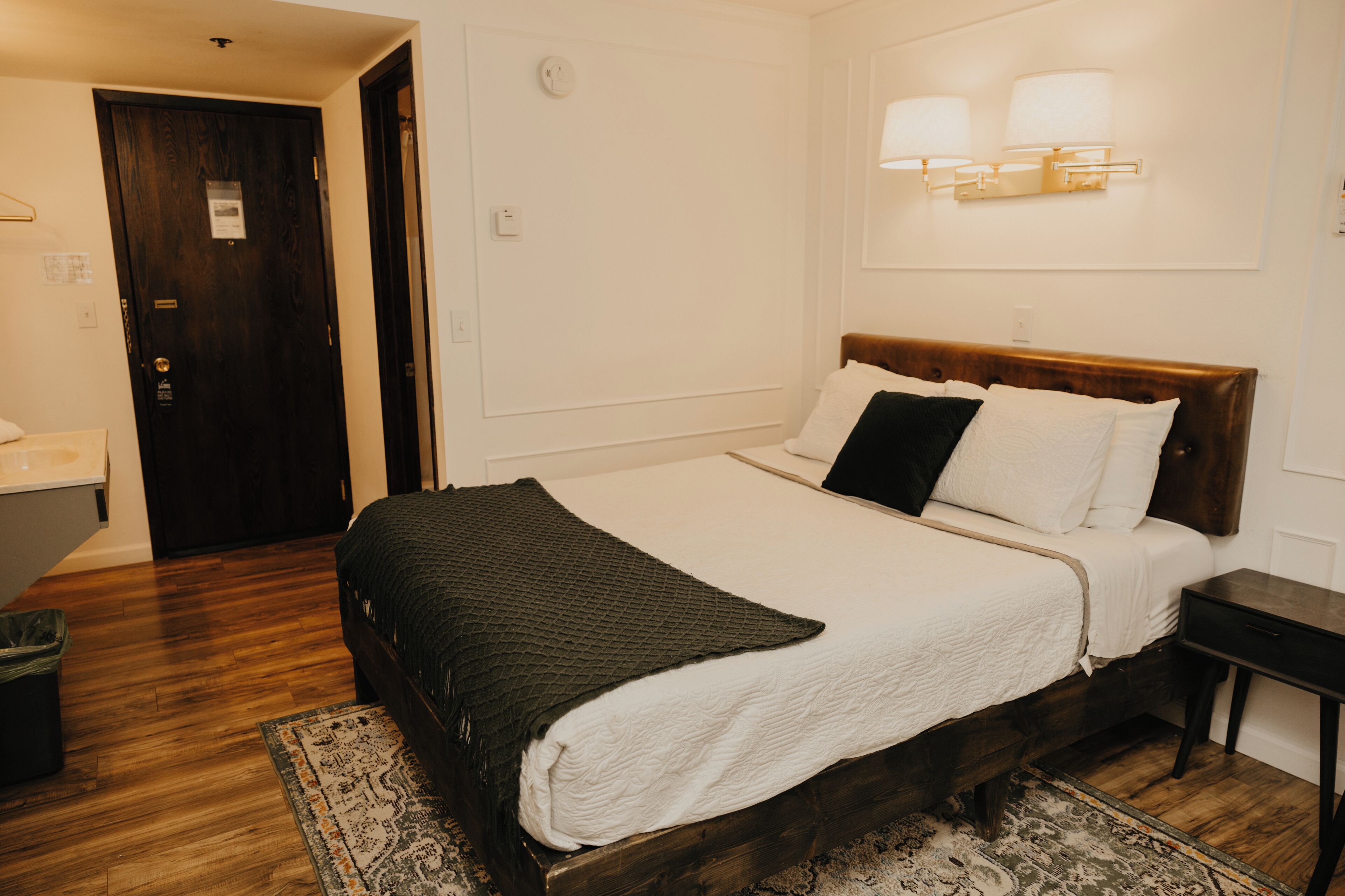 Un dormitorio con cama de madera, ropa de cama blanca, cabecera oscura y mesita de noche.