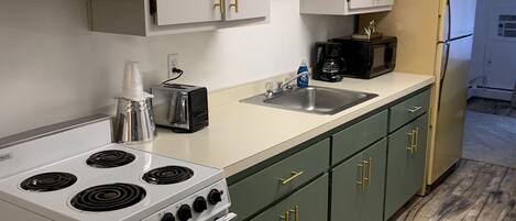 A kitchen with white cabinets, a stove, a microwave, and a refrigerator.