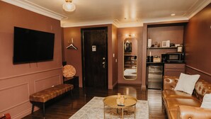 A modern living room with a flat-screen TV, a bench, a coffee table, and a brown leather sofa. - The Brooks Hotel (Wallace)