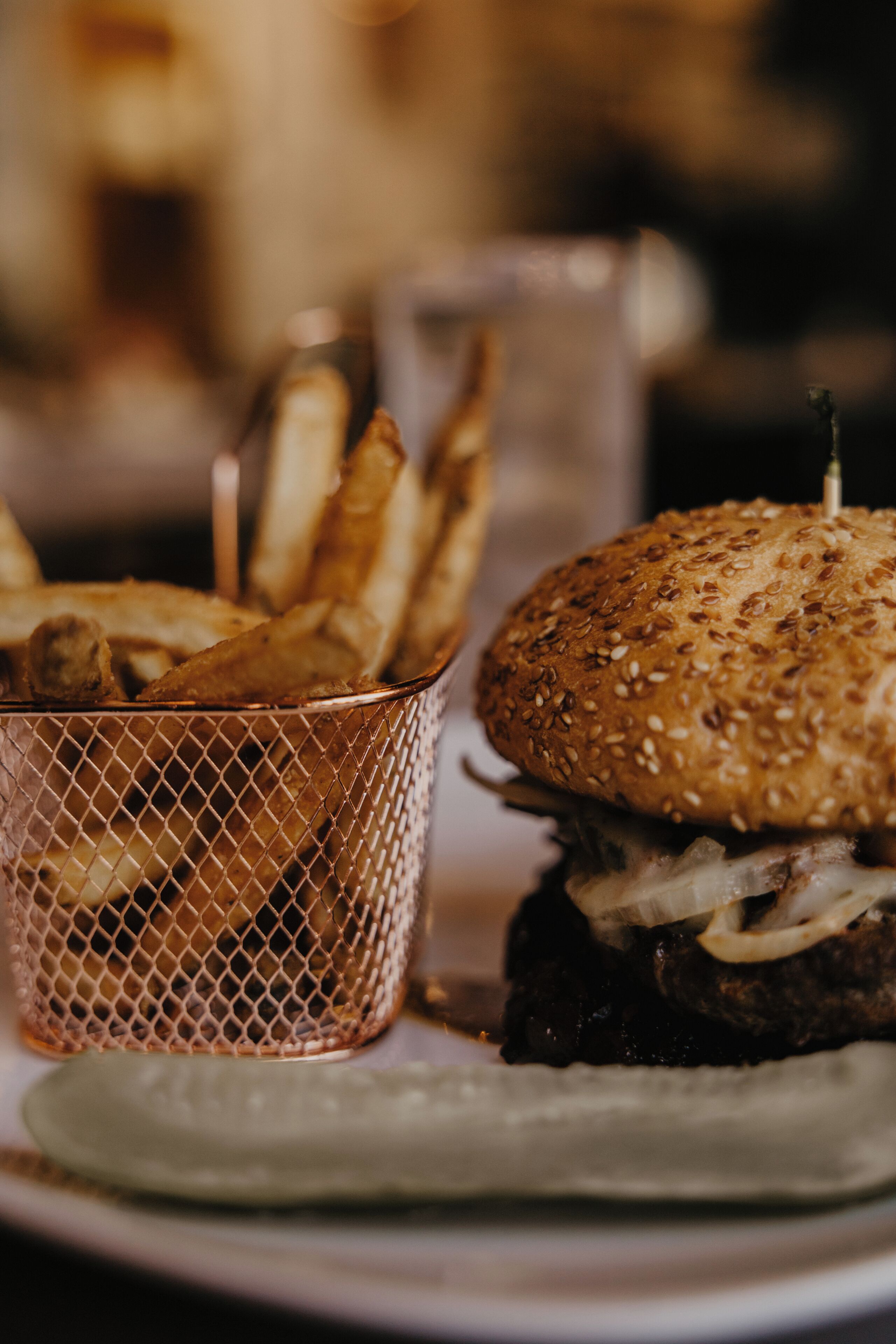 En hamburgare med ett sesamfröbröd och en portion pommes frites serverade i en korg.