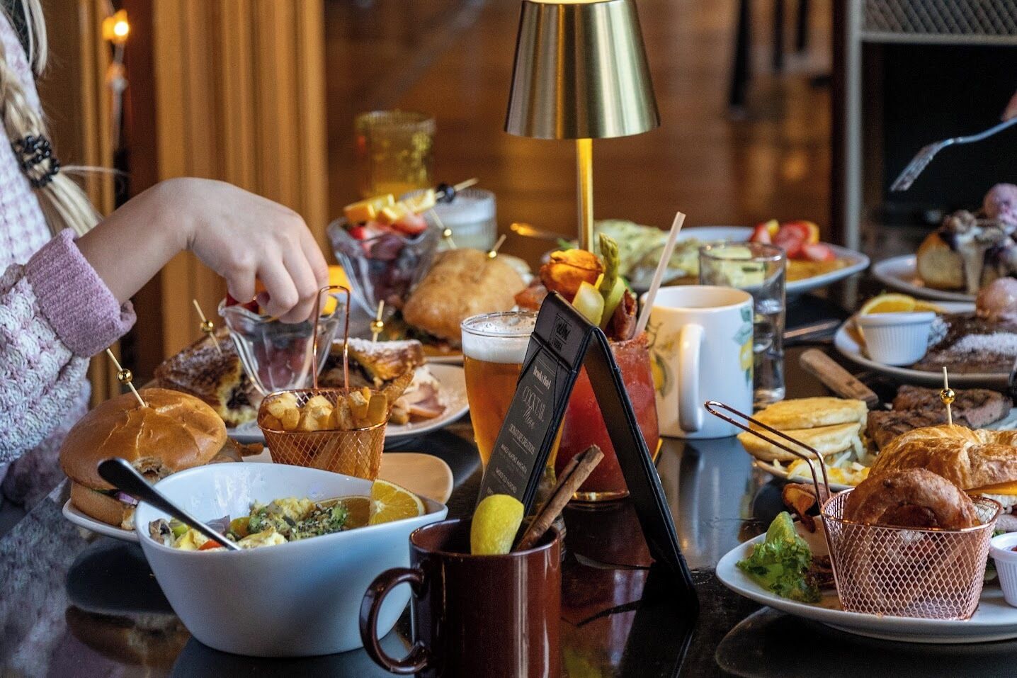 A table set with various dishes, drinks, and a cocktail menu stand.