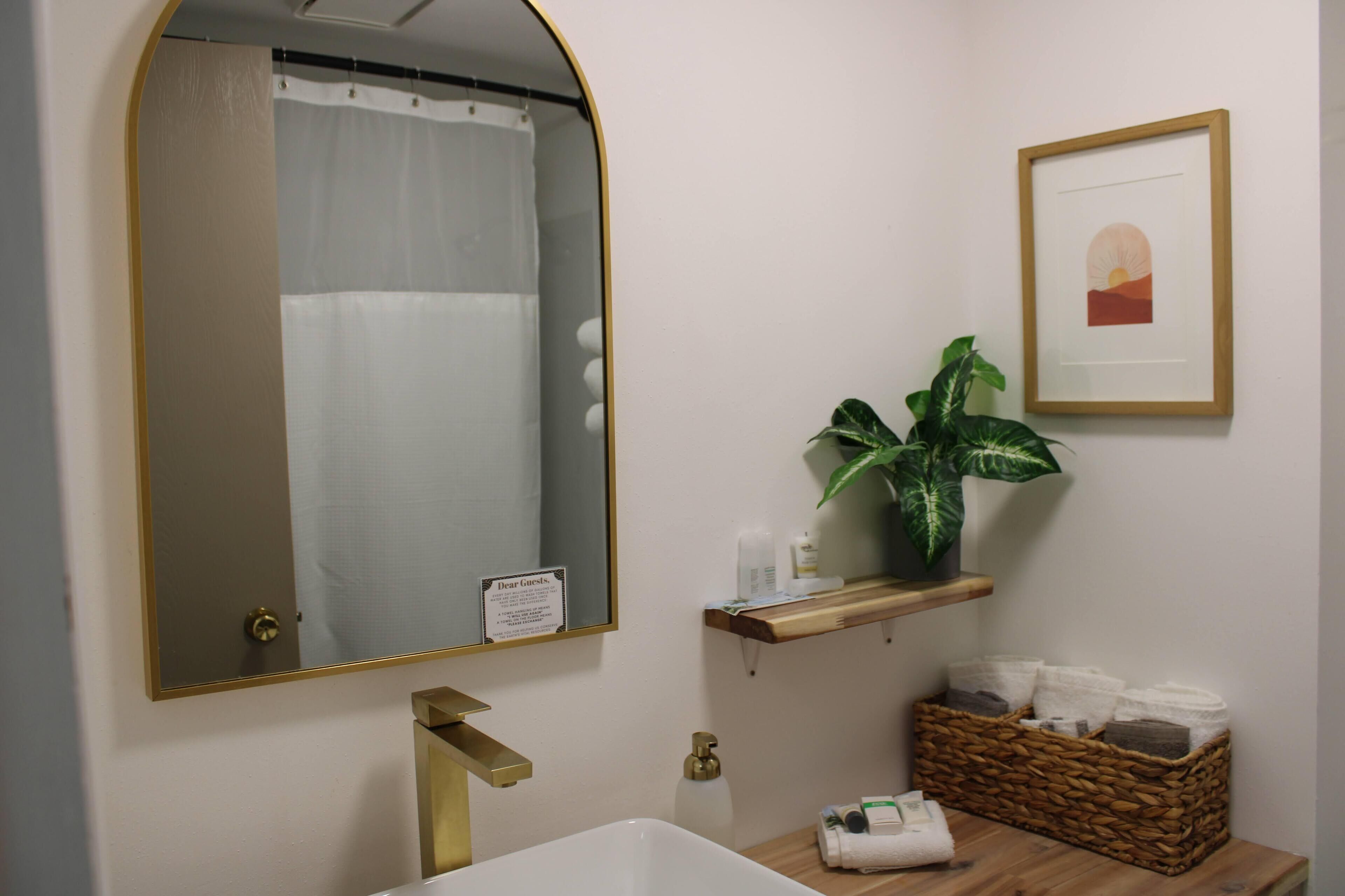 A bathroom with a large mirror, a shower curtain, a sink, a plant, and a framed picture on the wall.
