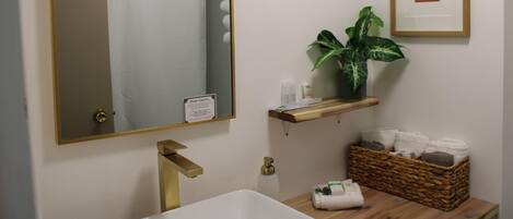 A bathroom with a large mirror, a shower curtain, a sink, a plant, and a framed picture on the wall.