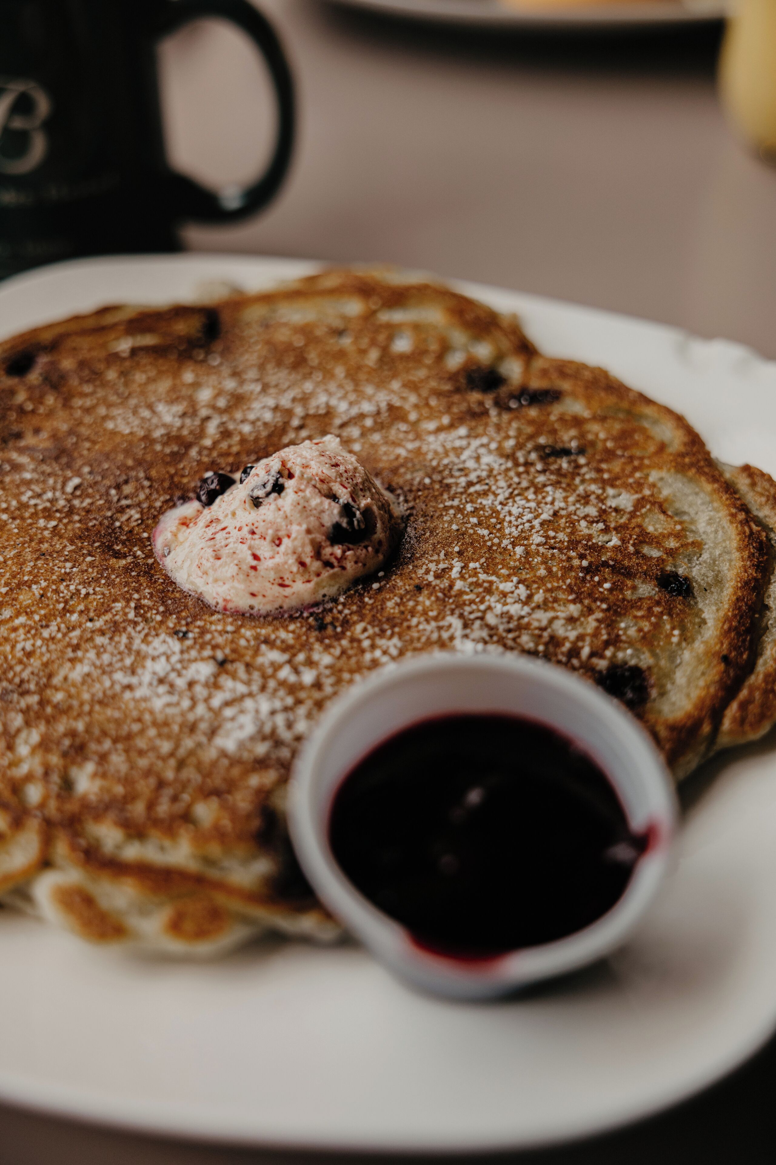A stack of pancakes with syrup and powdered sugar on a plate.