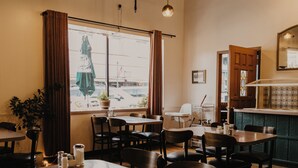 A cozy restaurant interior with wooden tables and chairs, hanging pendant lights, and a view through the window. - The Brooks Hotel (Wallace)