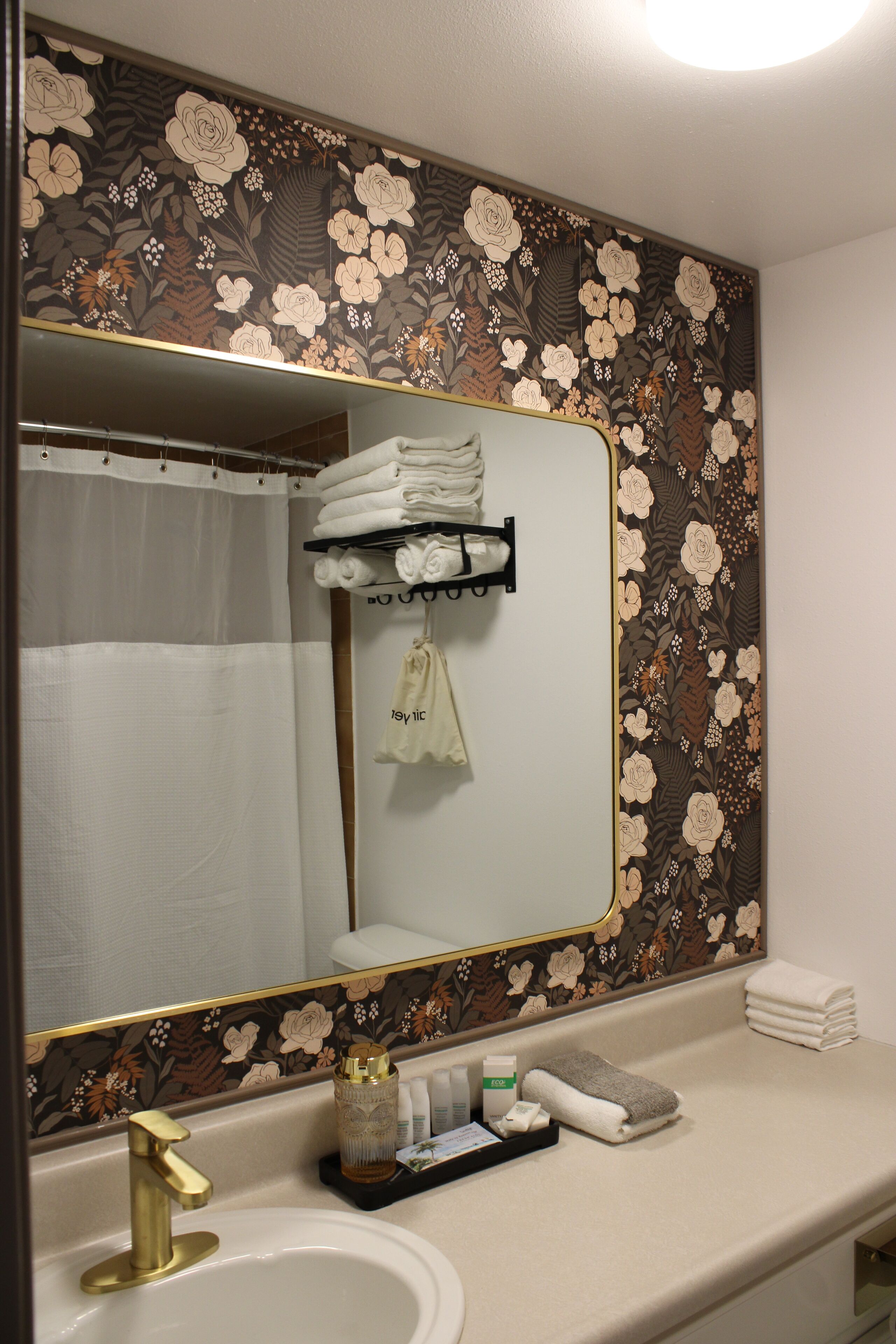 Une salle de bain avec un papier peint à motifs floraux, un robinet doré et un porte-serviettes sur lequel sont pliées des serviettes.