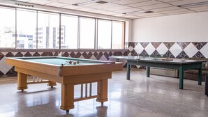 Ein Billardtisch mit grüner Spielvliesdecke und Holzrahmen, in einem Raum mit großen Fenstern und einer Fliesenwand.