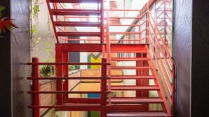 Eine rote Metalltreppe, die zu einer oberen Ebene führt, mit Blick auf einen Innenraum eines Gebäudes und einer Tür mit einem gelben 'M'-Schild.