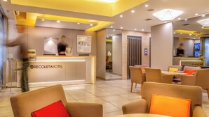 Eine Hotelhalle mit Rezeption, Sitzgelegenheiten und einem sichtbaren Aufzug.