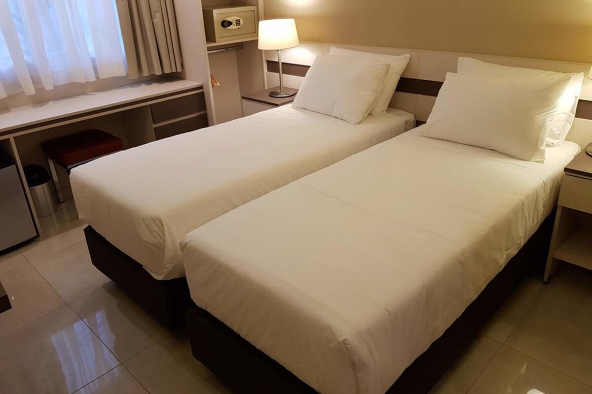 A hotel room with two beds, a desk, a chair, a lamp, and a safe.