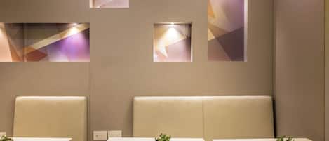 Un interior moderno con tres mesas blancas, cada una con una pequeña planta encima. Las paredes tienen paneles de luz geométricos.