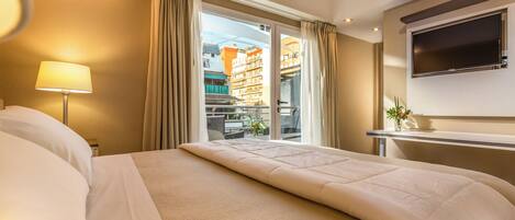 Habitación de hotel con una cama grande, un televisor montado en la pared y un balcón con vistas a edificios.