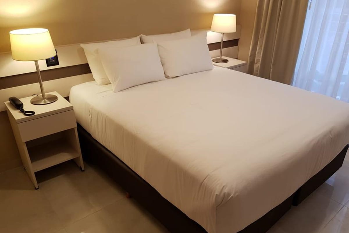 A neatly made bed with white linens, two bedside lamps, and a telephone on a bedside table.