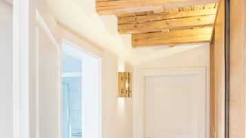A hallway with wooden ceiling beams, a white door, and a glass shower area visible through an open door.