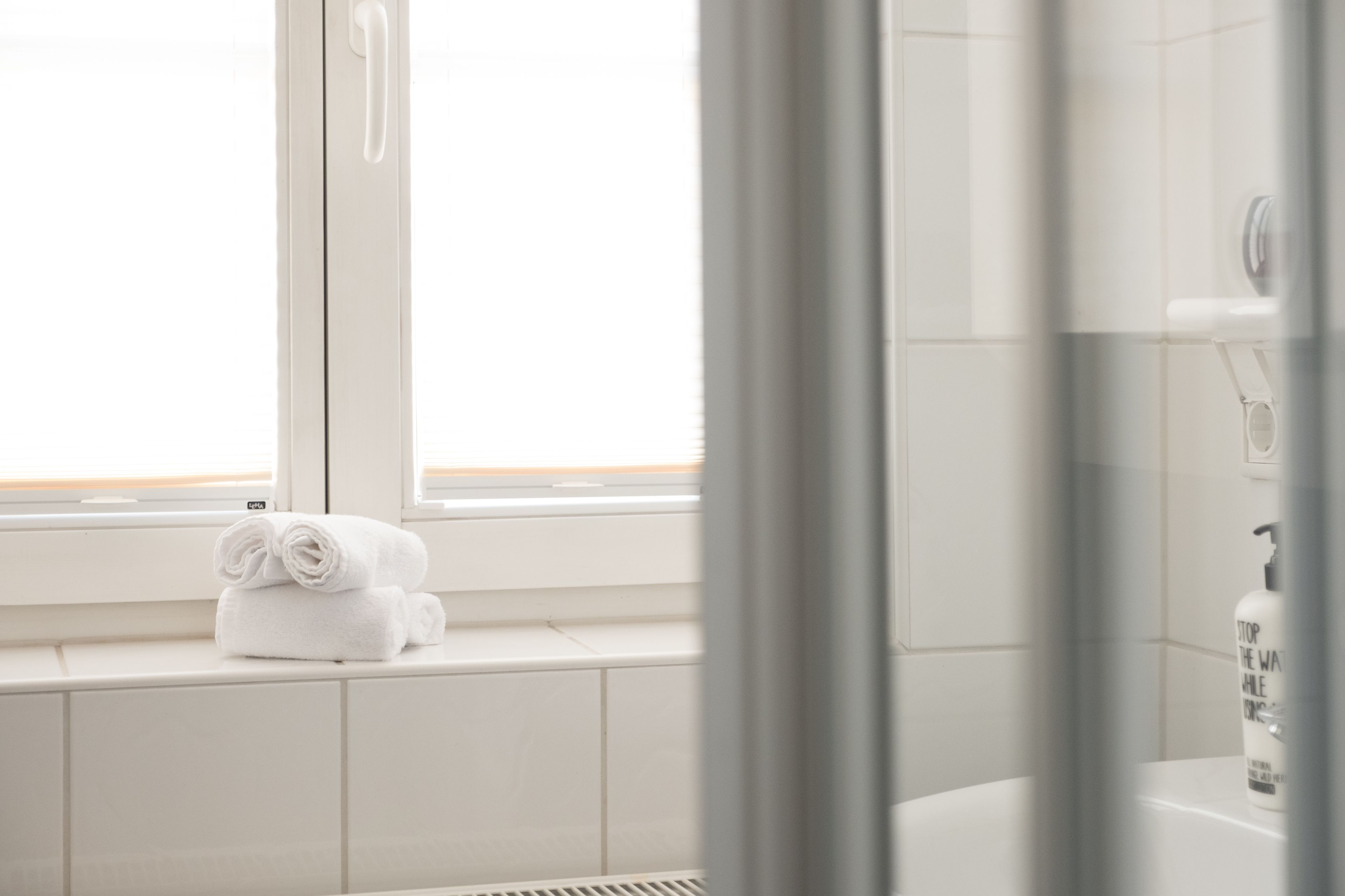 Un baño con ventana, una toalla en el alféizar y una botella en el lavamanos.