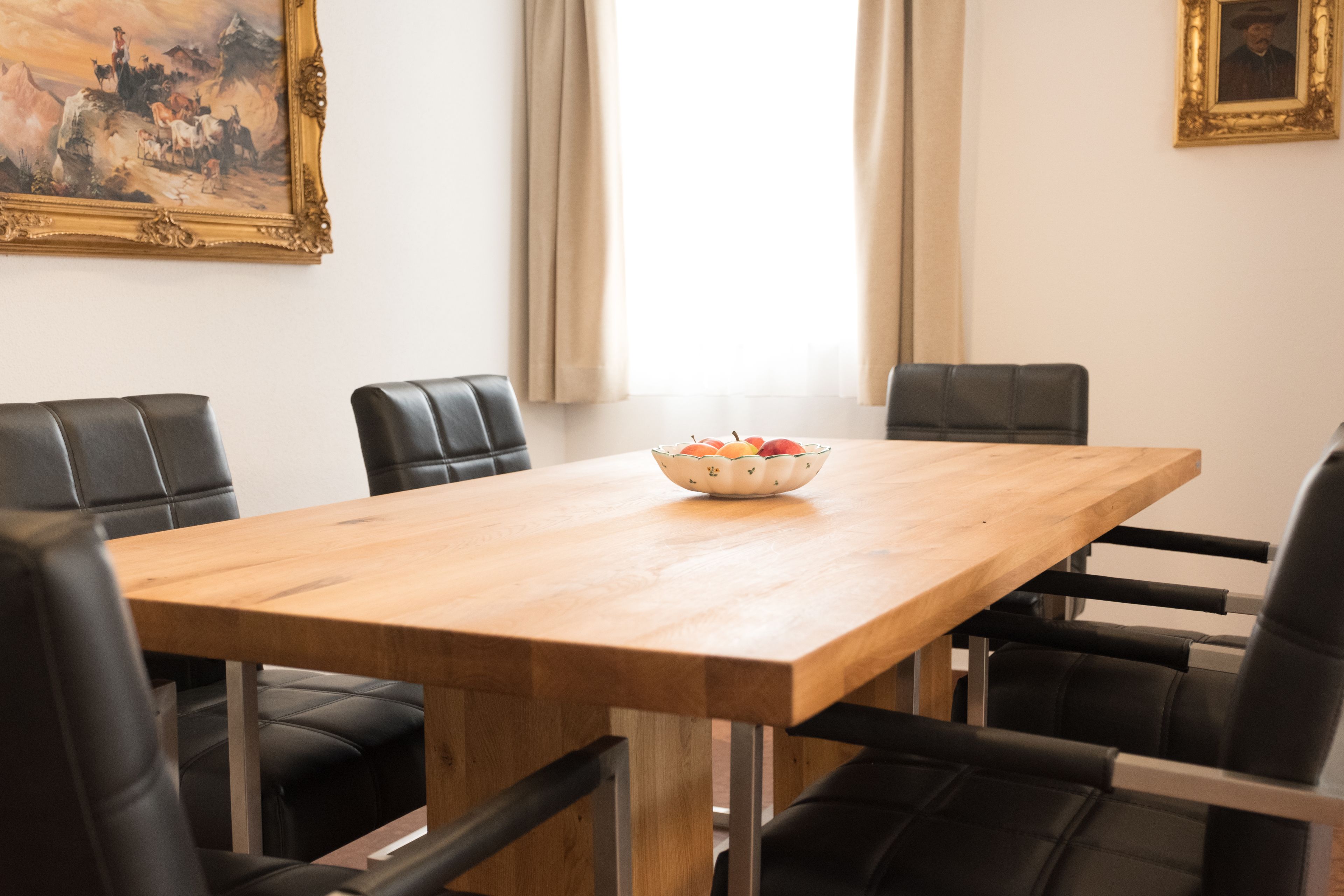 Una sala de conferencias con una mesa de madera, sillas de cuero negro, un frutero y un cuadro enmarcado en la pared.