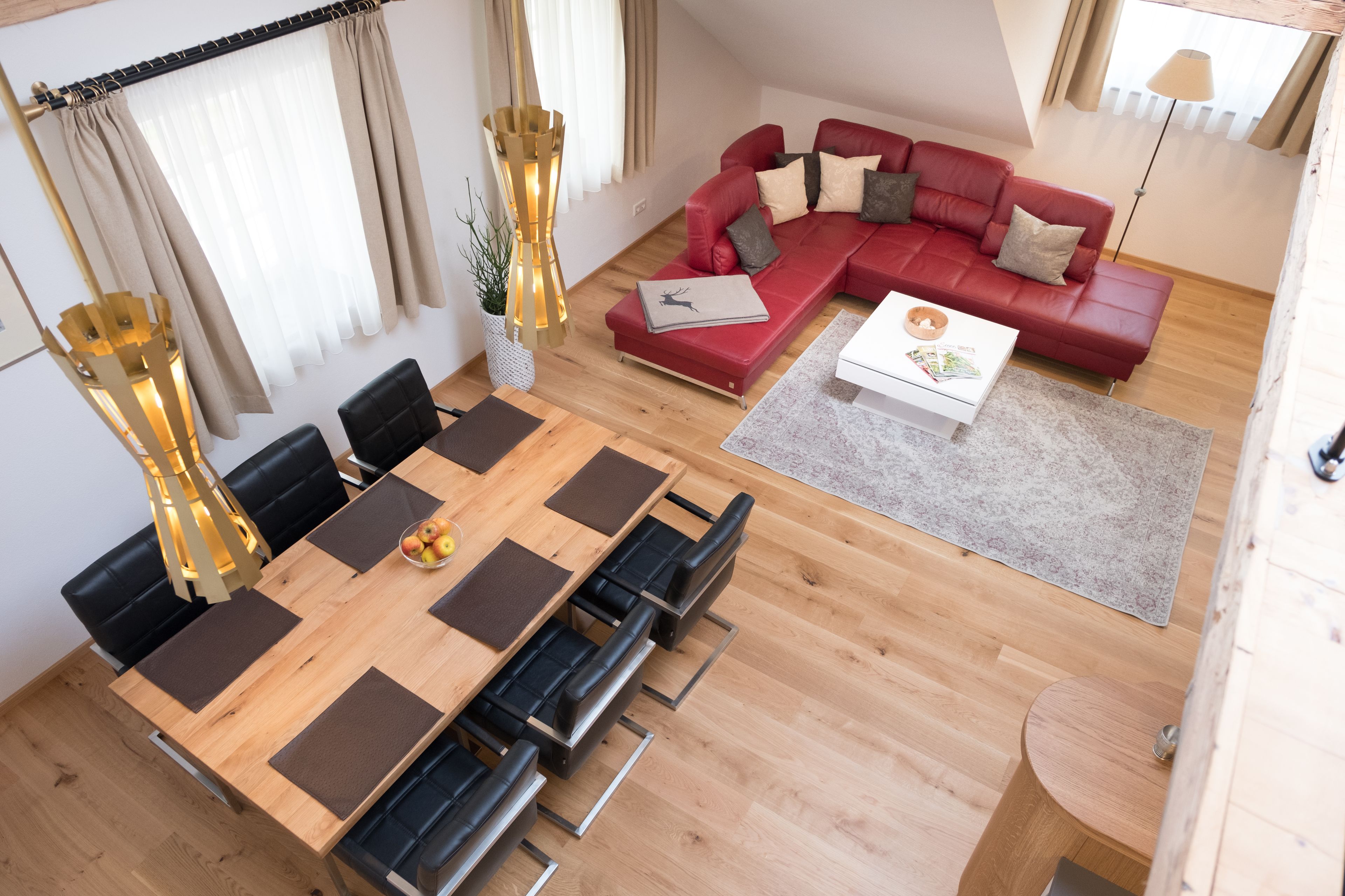 Una sala moderna con un sofá seccional rojo, una mesa de comedor de madera con sillas negras y una pequeña mesa redonda con una lámpara.