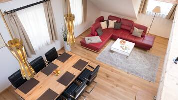 Una sala moderna con un sofá seccional rojo, una mesa de comedor de madera con sillas negras y una pequeña mesa redonda con una lámpara.