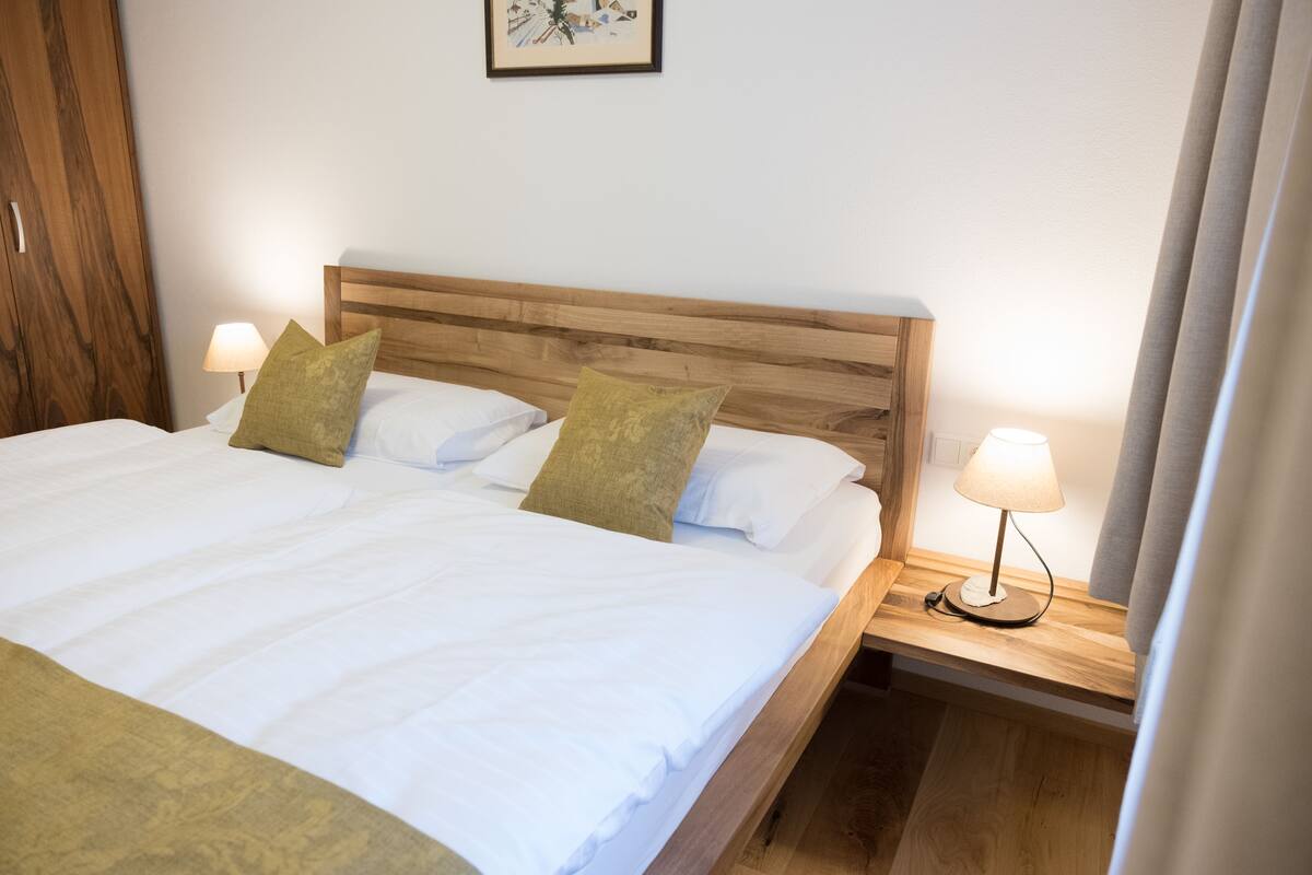 A neatly made bed with white linens and two pillows, a wooden headboard, and two bedside lamps on wooden nightstands.