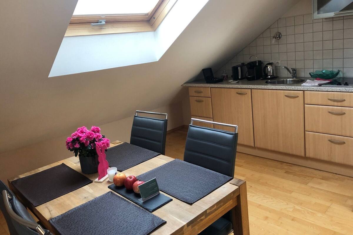 A dining area with a table set for two, a small potted plant, and a laptop.