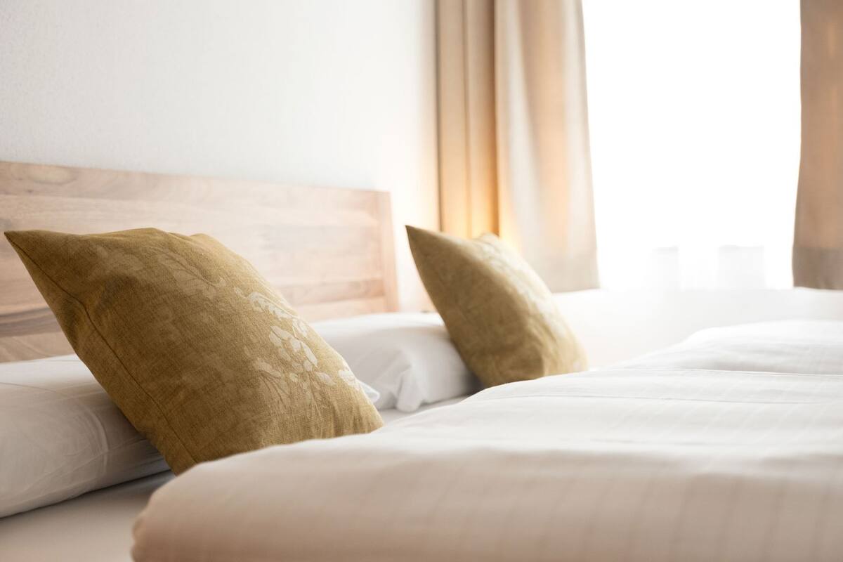 A bed with white bedding and two pillows, a wooden headboard, and a window with curtains.