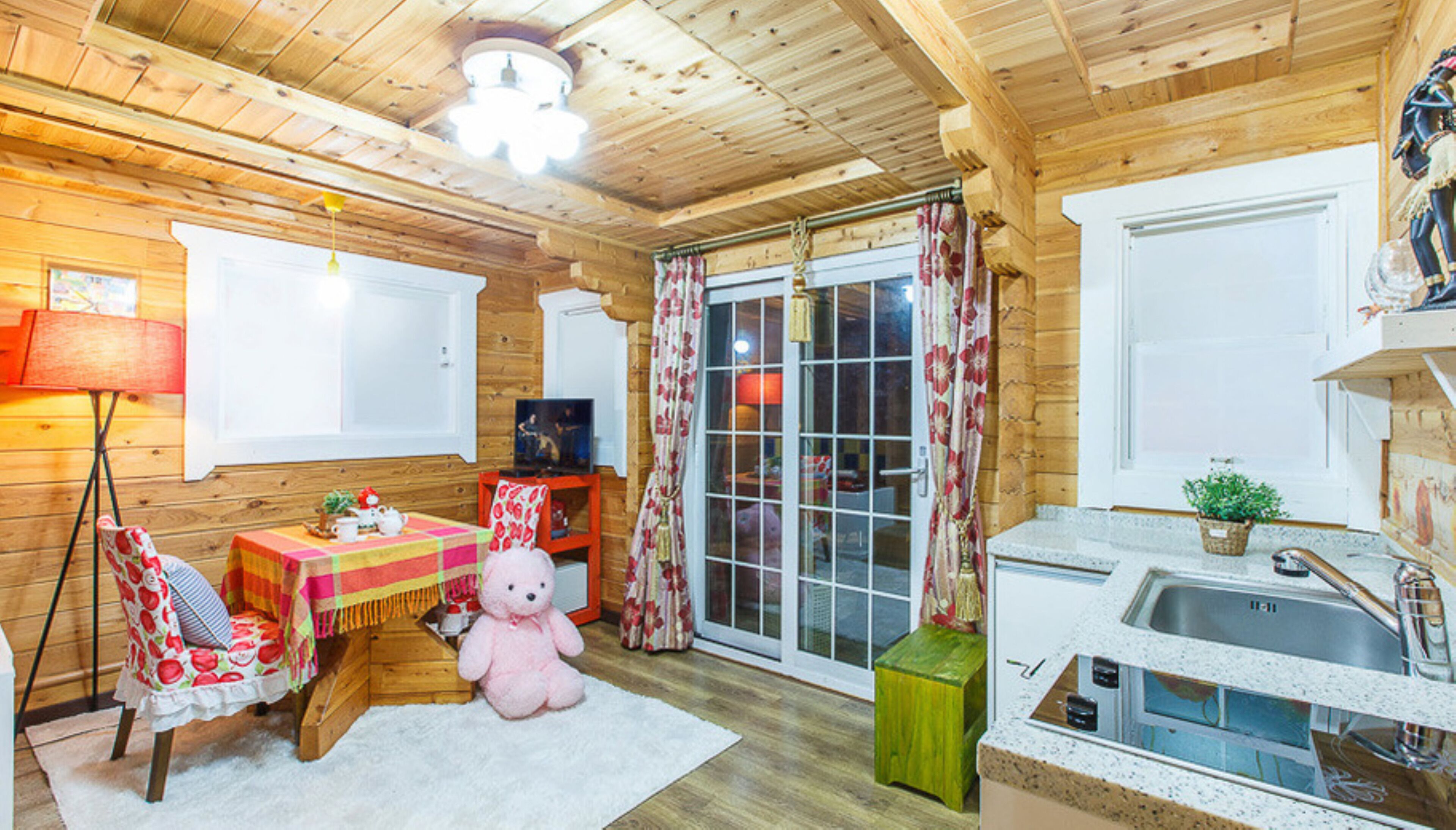 Ein gemütliches Blockhaus-Interieur mit Holzausstattung, einem Essbereich mit Tisch und Stühlen, einem Teddybären und einer Küche mit Spüle und Schränken.