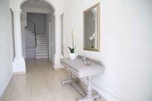 A hallway with a white staircase, a white column, a white vanity with a mirror, and a potted orchid. - Valletta Luxury Harbour View (Valletta)
