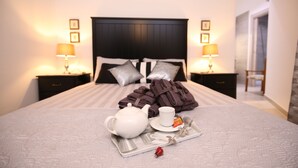A neatly made bed with a tray of breakfast items, including a teapot, cup, and towels.