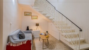 A modern living room with a staircase, a red sofa, a small wooden table, and a lamp.