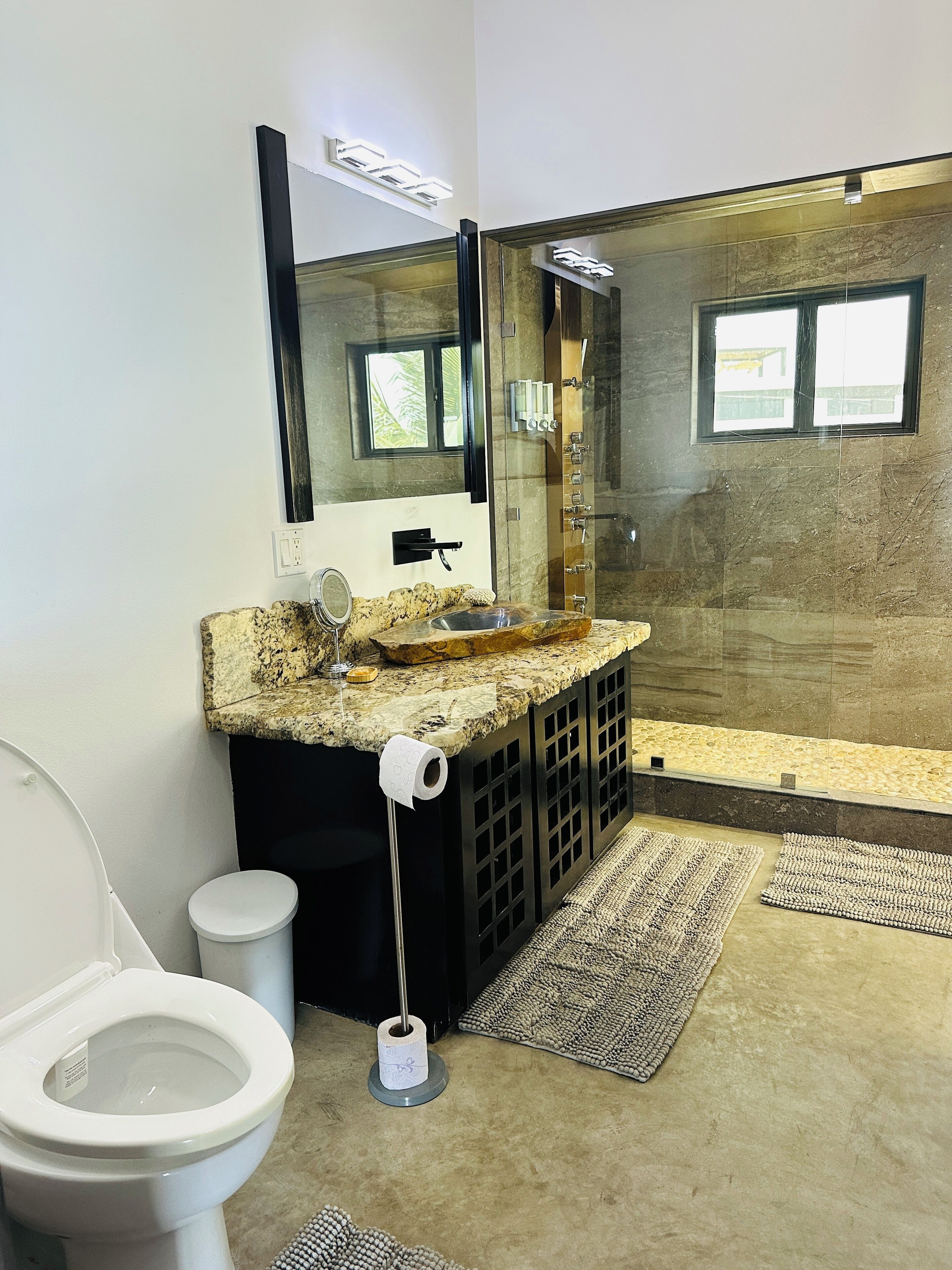 A modern bathroom with a glass-enclosed shower, a granite countertop, and a toilet.